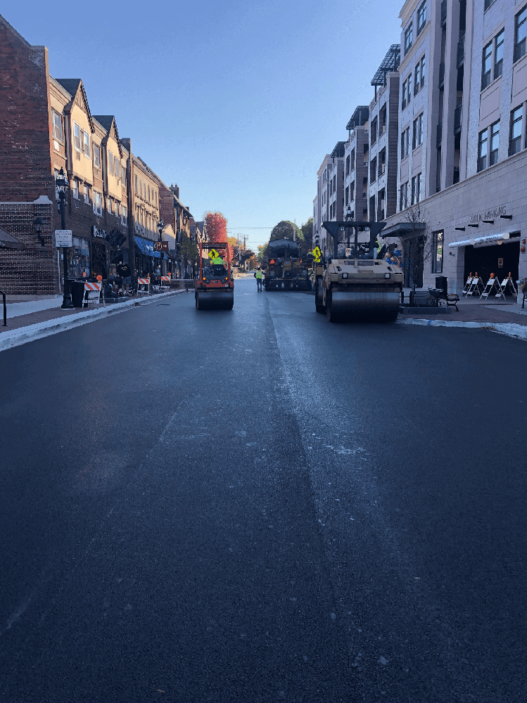 Roadway Construction and Asphalt Paving in Downtown Area with ALAMP Crew Members and Vehicles in Background