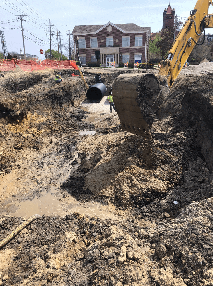 Concrete Construction with Sewer and Water Infrastructure in Downtown Area with ALAMP Crew Members and Excavator in Background