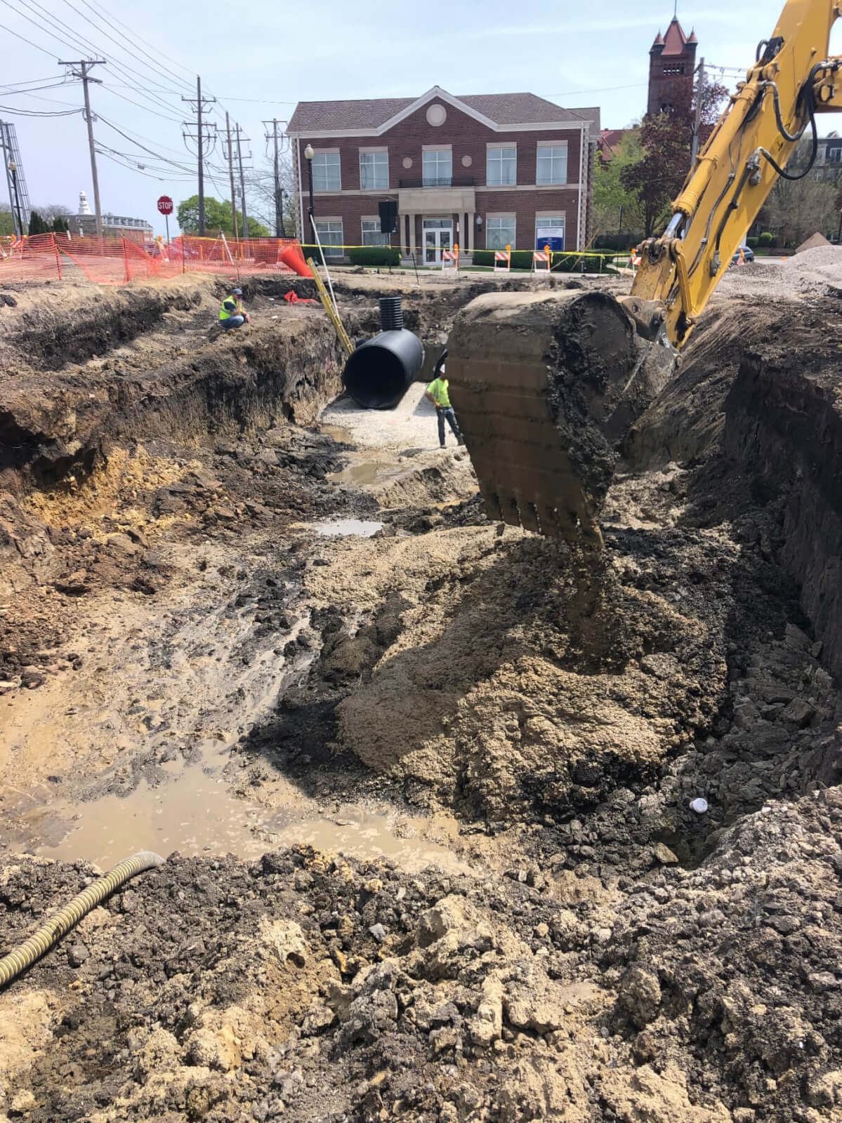 Concrete Construction with Sewer and Water Infrastructure in Downtown Area with ALAMP Crew Members and Excavator in Background